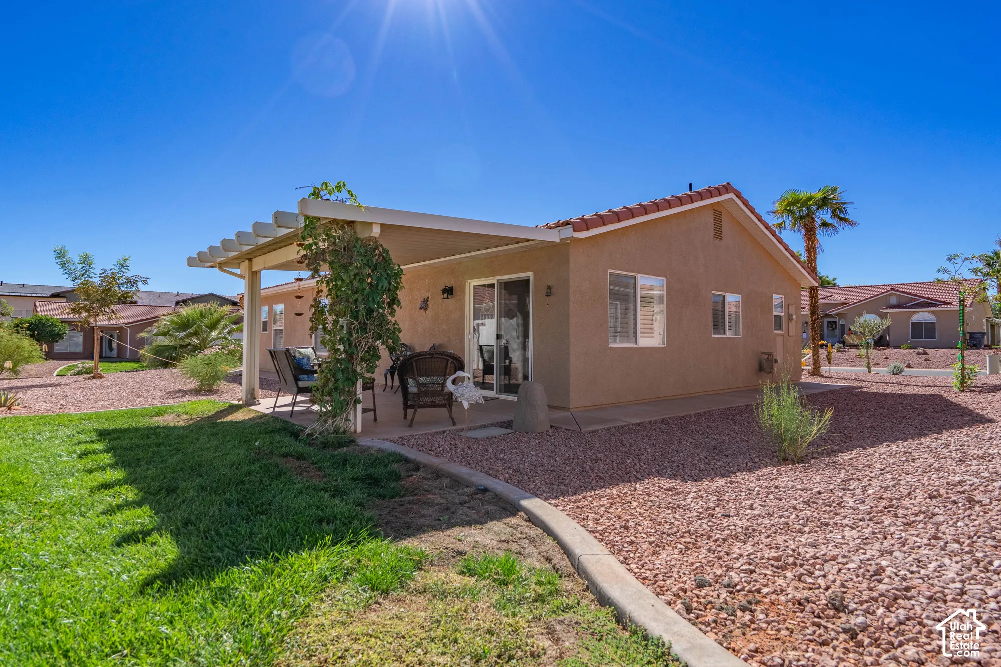 Stucco exterior with a tile roof, featuring a covered patio, sliding glass door, and a partially grassed and rock-landscaped yard