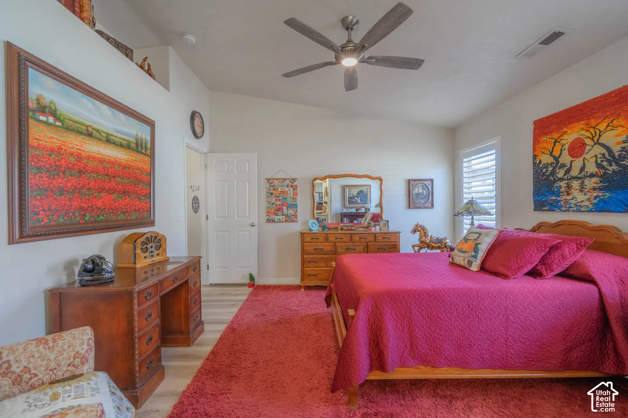 Vaulted ceiling, wood-finish flooring, ceiling fan with integrated lighting, door with panel detailing, and window with white louvered shutters