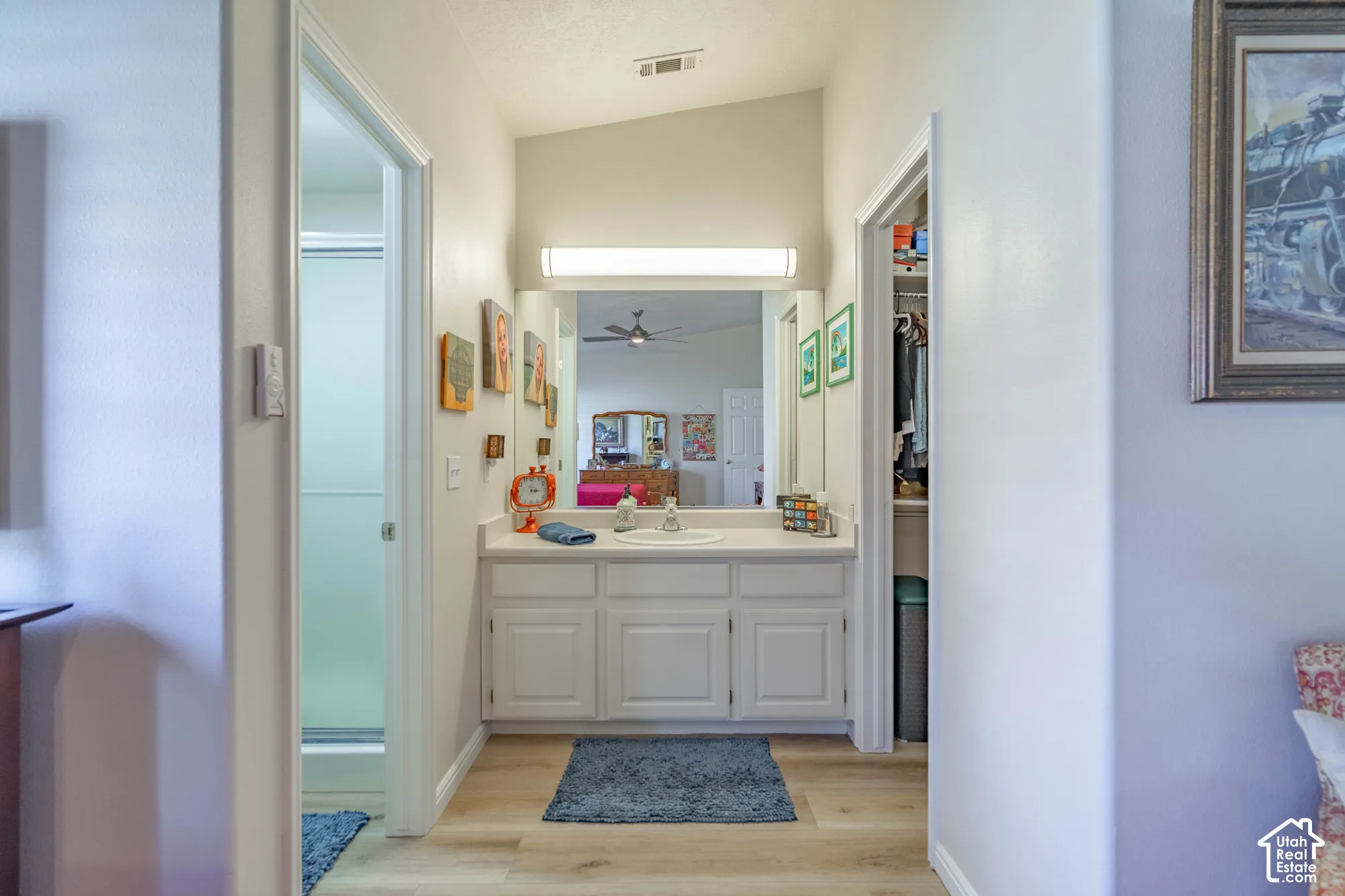 White vanity with integrated sink, overhead lighting, wood-finish flooring, and a mirrored wall