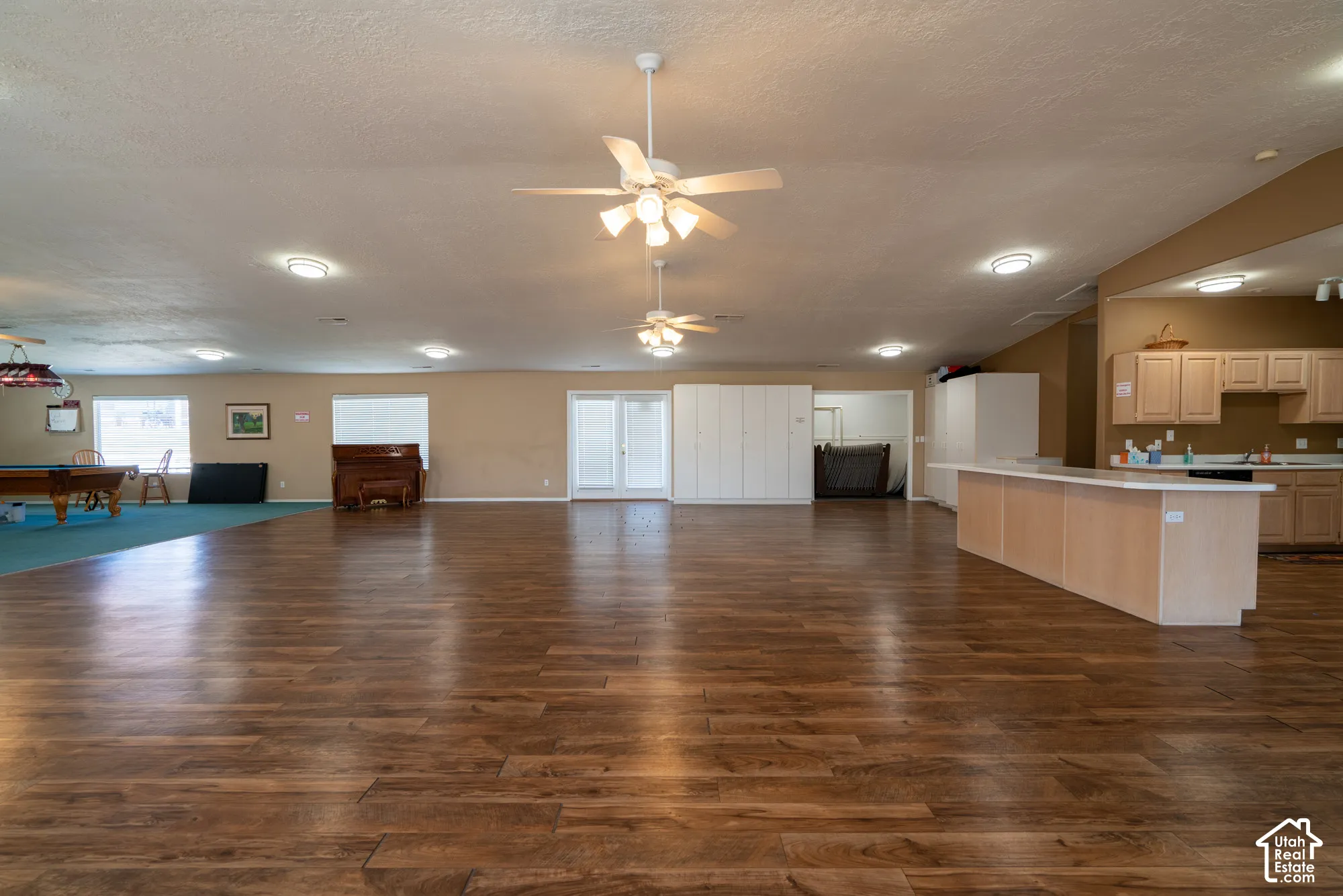 Expansive open-concept room featuring wood-finish flooring, multiple ceiling fans, recessed lighting, and a built-in kitchen area with cabinetry and a large island