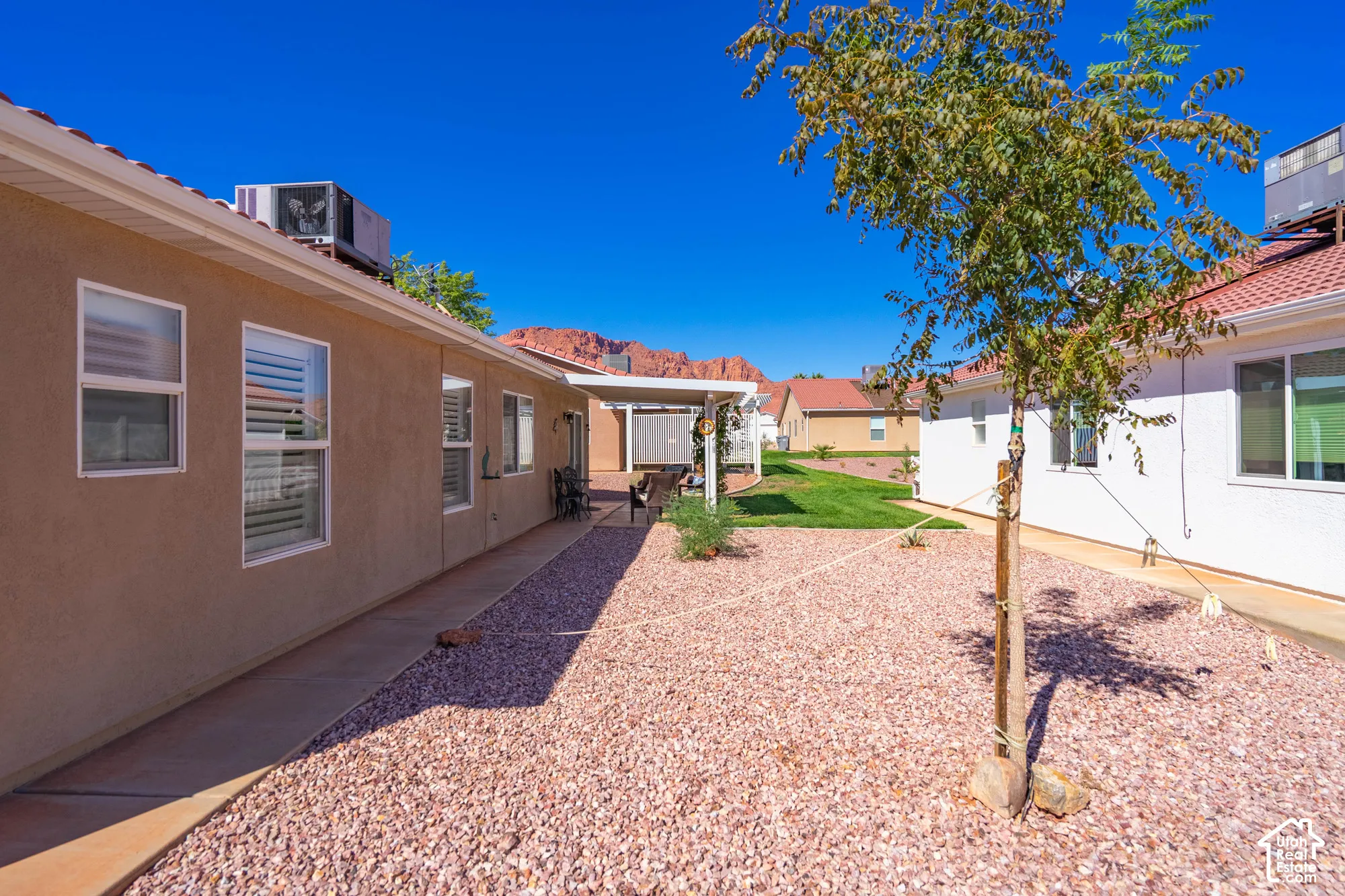 Brown stucco exterior with multiple windows, a concrete walkway, and gravel landscaping