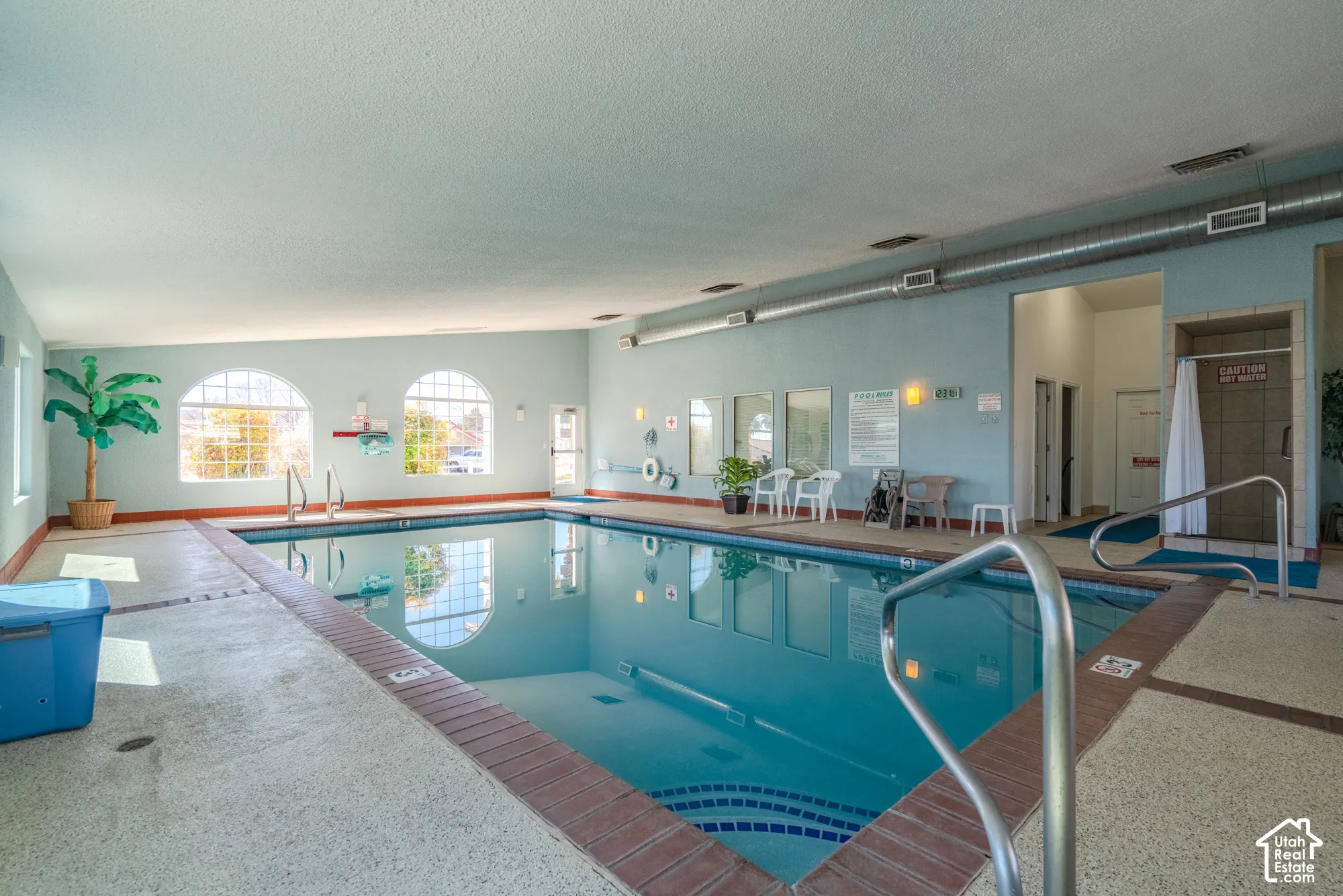 Indoor swimming pool with arched windows, tiled pool surround, and metal handrails