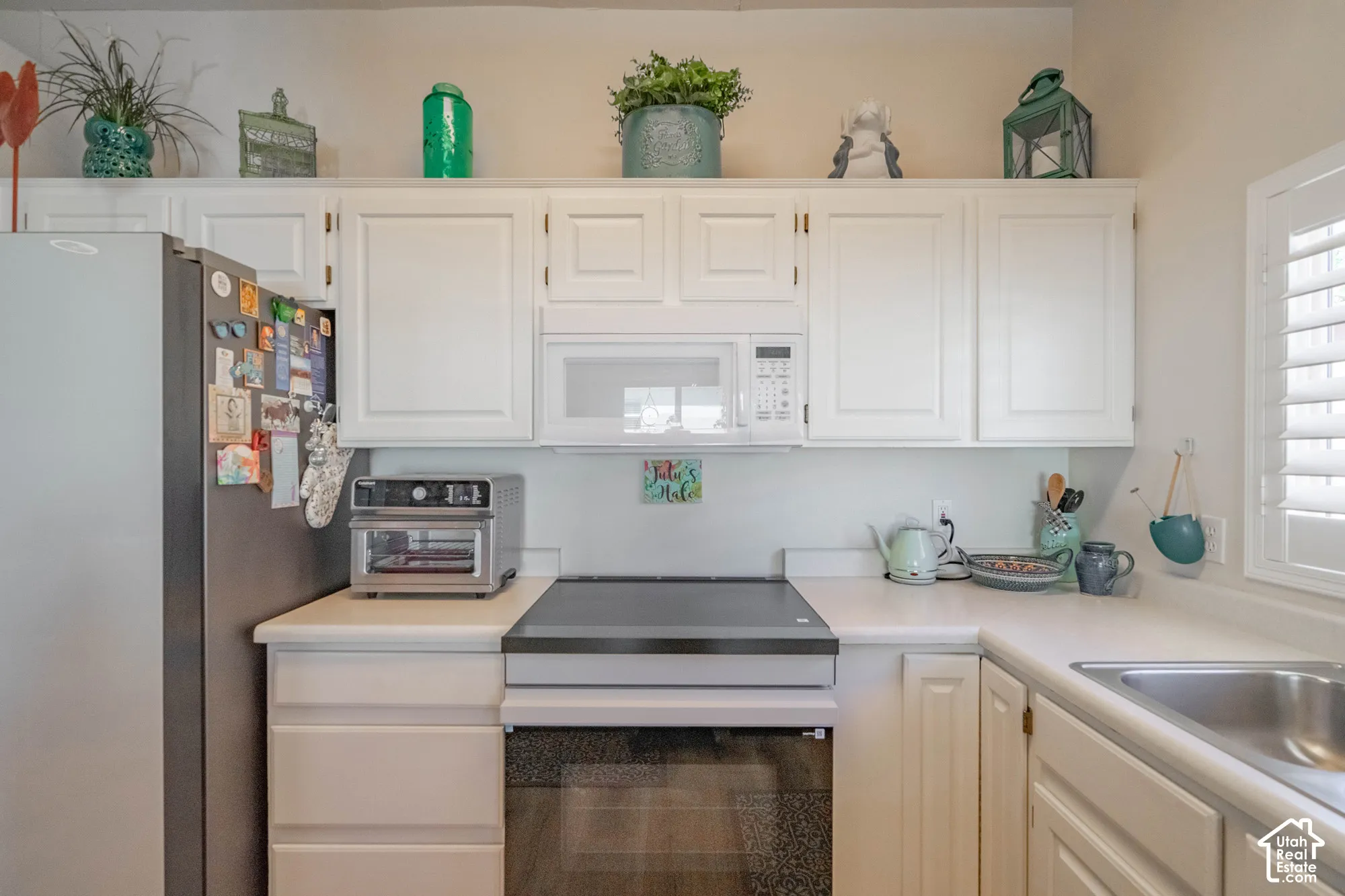 White cabinetry with upper display shelf, integrated microwave, built-in electric cooktop, stainless steel sink, and plantation shutters