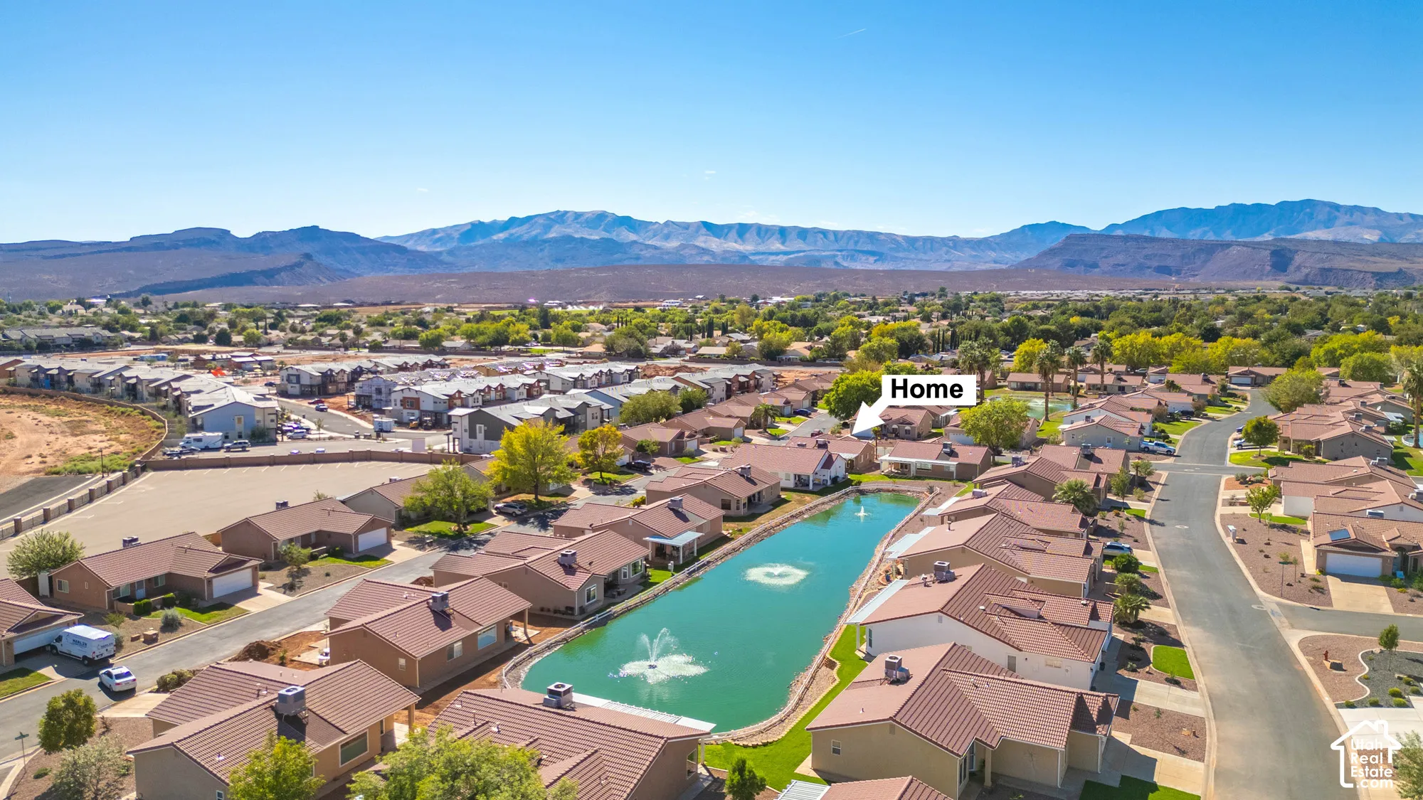 Community setting with a central pond featuring a fountain, surrounding residential properties, and distant mountain ranges