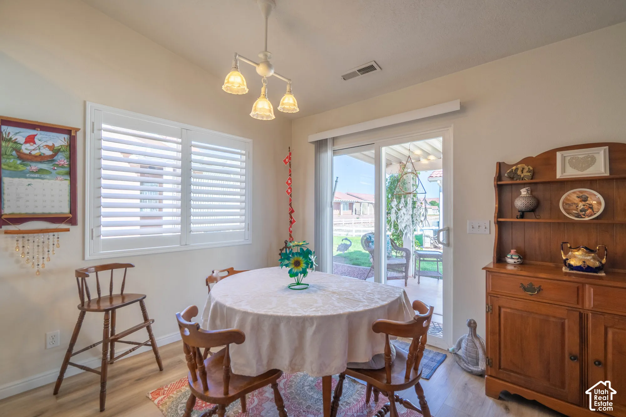 Vaulted ceiling, white plantation shutters, wood-finish flooring, sliding glass door, overhead light fixture