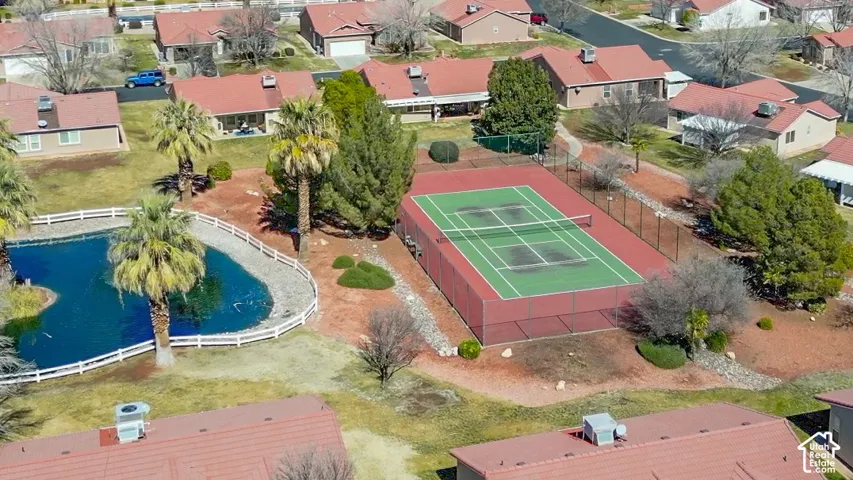 Community amenities featuring a tennis court, a pond with a white fence border, and mature palm trees