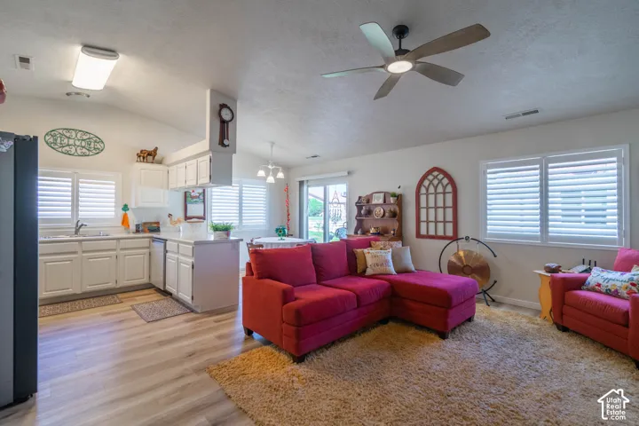 Open-concept living space featuring wood-finish flooring, white cabinetry, a kitchen island, and a ceiling fan with integrated lighting