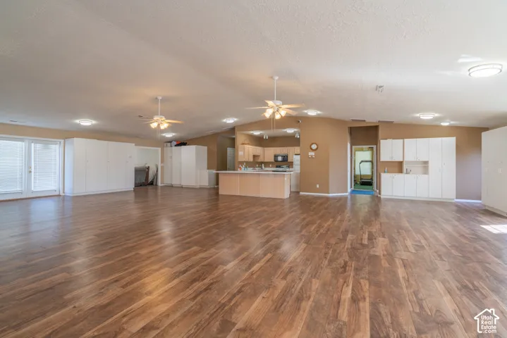 Expansive room featuring wood-finish flooring, white built-in cabinetry, dual ceiling fans, recessed lighting, and double glass doors