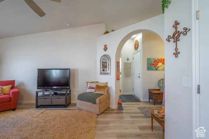 Vaulted ceiling, arched entryway, wood-finish flooring, white walls, and built-in ceiling fan