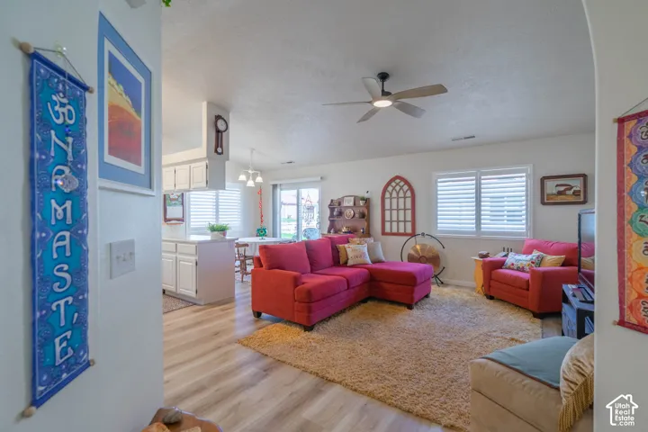 Vaulted ceiling with a ceiling fan, wood-finish flooring, white plantation shutters, white kitchen cabinetry, and a sliding glass door