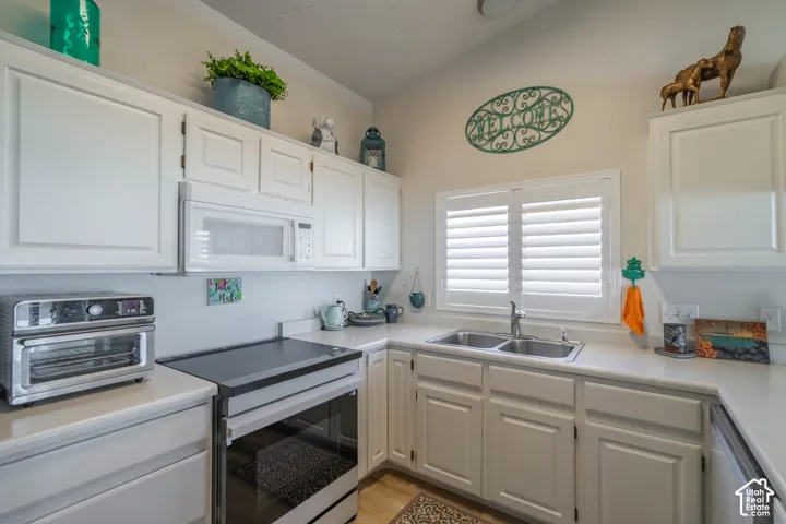 White cabinetry with brushed nickel hardware, solid surface countertops, double basin stainless steel sink, over-the-range microwave, and a built-in range