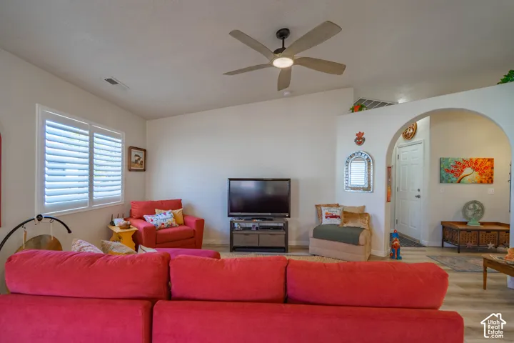 Vaulted ceilings, plank flooring, ceiling fan with integrated lighting, arched doorways, and window with plantation shutters