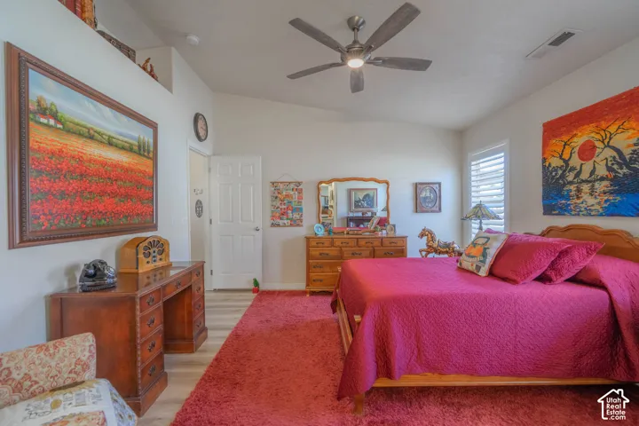 Vaulted ceiling, wood-finish flooring, ceiling fan with integrated lighting, door with panel detailing, and window with white louvered shutters