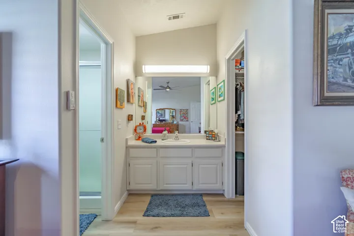 White vanity with integrated sink, overhead lighting, wood-finish flooring, and a mirrored wall