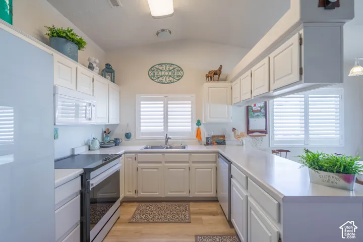 U-shaped kitchen with white cabinetry and countertops, integrated stainless steel sink, built-in microwave, and wood-finish flooring