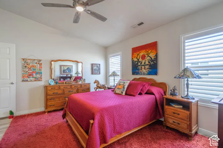 Vaulted ceiling, ceiling fan with integrated lighting, window treatments, wood-finish flooring, and white interior door
