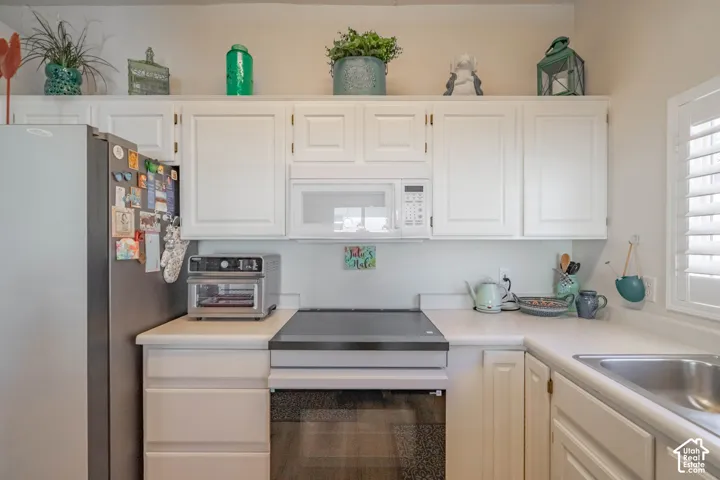 White cabinetry with upper display shelf, integrated microwave, built-in electric cooktop, stainless steel sink, and plantation shutters