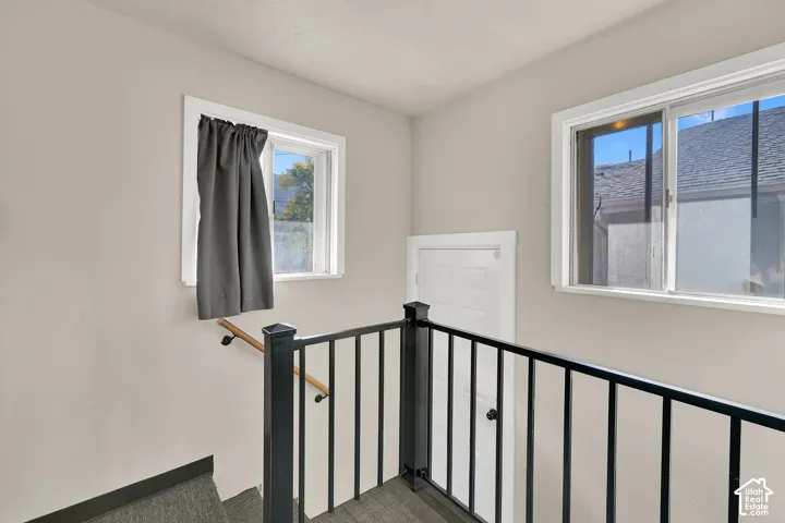 Black metal stair railing with a wood-finish handrail, white trim windows, and light-toned walls