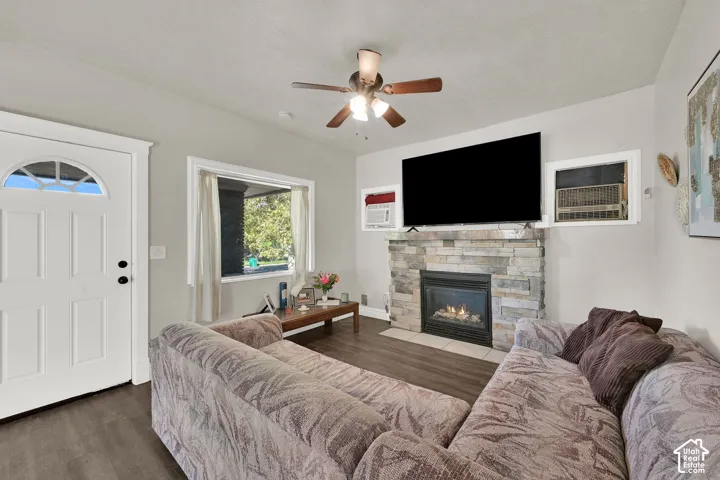 Wood-finish flooring, stone-clad fireplace with hearth, white paneled entry door with arched transom, ceiling fan with integrated lighting, and white trim