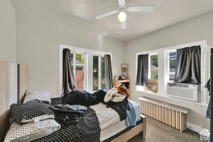 Bright bedroom with multiple windows featuring black-out curtains, wood-finish flooring, and a ceiling fan with integrated lighting
