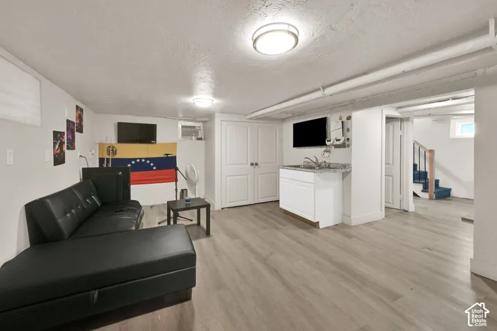 Wood-finish flooring throughout, featuring a built-in wet bar with a countertop and sink, and a staircase with a dark wood-finish handrail