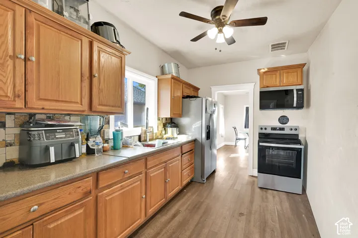 Kitchen featuring wood cabinetry, stainless steel appliances, wood-finish flooring, a ceiling fan, and a window for natural light