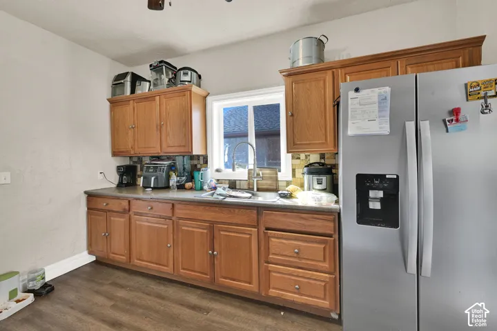 Wood-finish flooring, wood cabinetry with upper and lower storage, laminate countertops, and a stainless steel refrigerator with an external ice/water dispenser