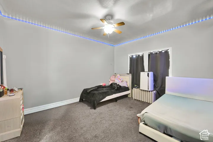 Spacious bedroom with neutral carpet flooring, ceiling fan with integrated lighting, and ample room for multiple bed configurations