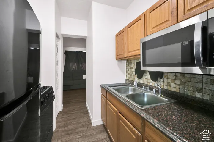 Galley kitchen featuring wood-finish cabinetry, granite-style countertops, stainless steel appliances including a microwave hood and under-counter sink, and tile backsplash