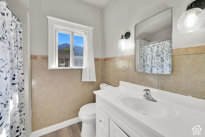 White vanity with integrated sink, chrome faucet, wall-mounted mirror, and tile wainscoting