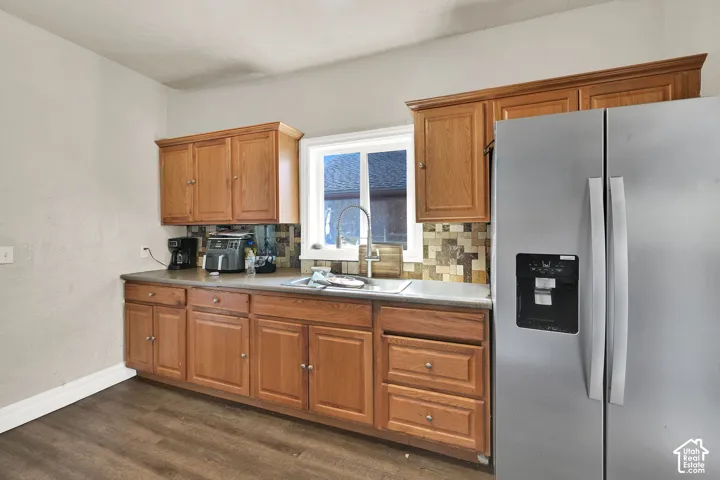 Kitchen featuring warm wood cabinetry with multiple storage options, stainless steel French-door refrigerator with ice and water dispenser, gas cooktop with tile backsplash, and dark wood-finish flooring throughout