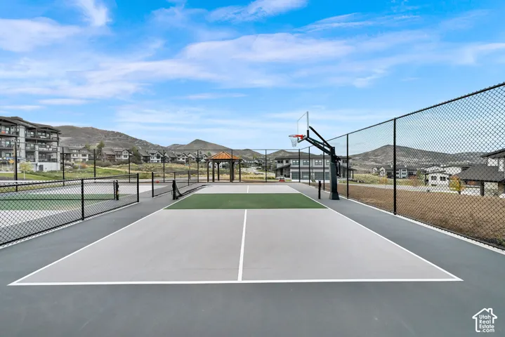 Multi-sport court featuring dedicated basketball and pickleball areas, a chain-link perimeter fence, and a distant gazebo