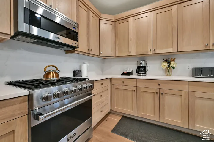 Stainless steel range, wood-finish cabinetry, white countertops, tile backsplash, and wood-finish flooring