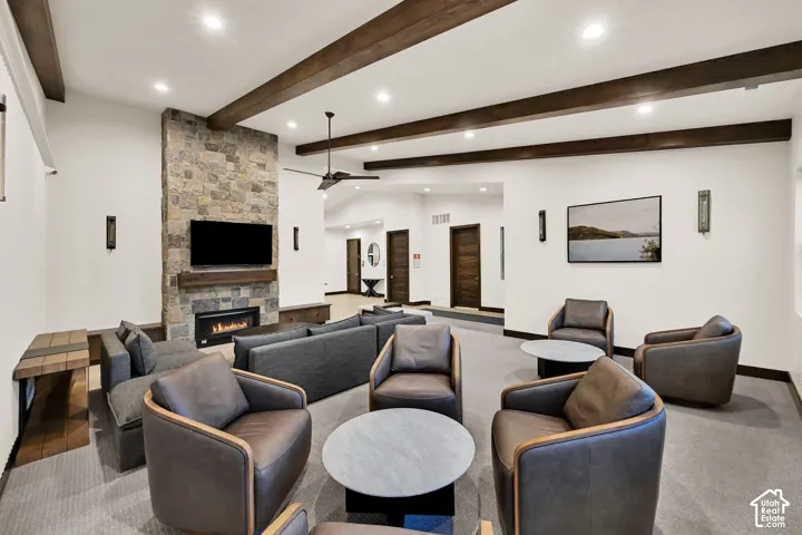 Stone-clad fireplace with a wood mantel, exposed ceiling beams, recessed lighting, and a ceiling fan