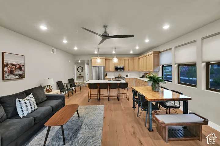Open-concept living space featuring wood-finish flooring, recessed lighting, a modern ceiling fan, and light wood cabinetry with stainless steel appliances