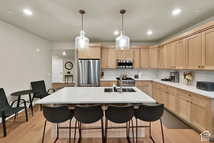 Kitchen featuring a center island with seating, stainless steel appliances, light wood-finish cabinetry, and recessed lighting