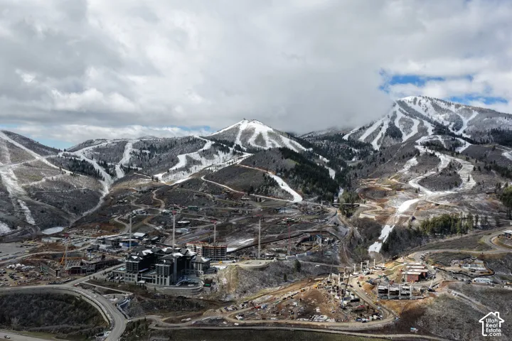 Mountainous terrain featuring snow-dusted peaks, established ski runs, modern architectural structures, and ongoing development sites
