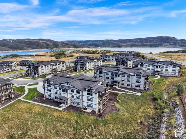 Modern multi-unit residential community featuring contemporary architectural design with mixed-material facades in charcoal and cream tones, expansive manicured grounds with native landscaping, and panoramic backdrop of rolling hills and water features