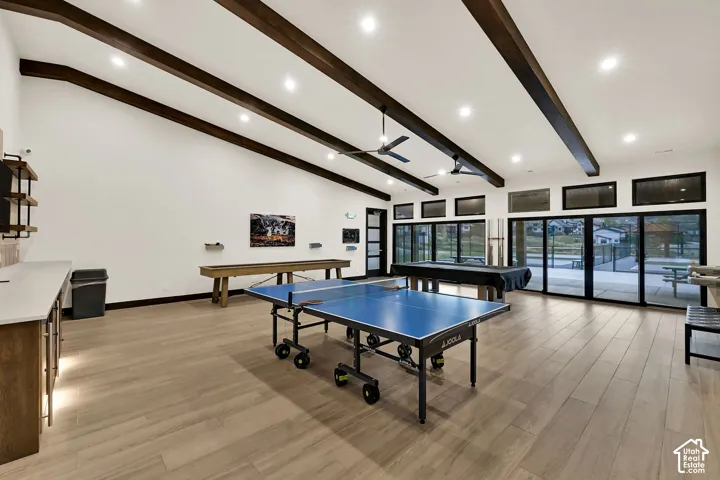 Vaulted ceilings with exposed beams, wood-finish flooring, recessed lighting, built-in shelving, and extensive glass doors