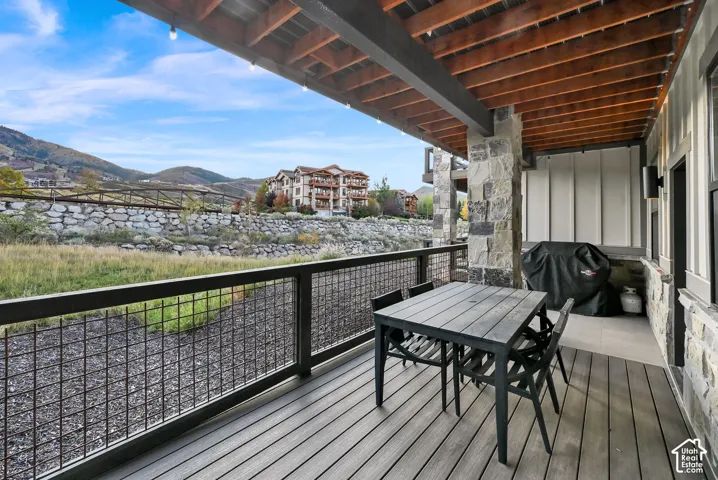 Expansive covered outdoor living space featuring composite decking, wood beam ceiling, stone pillars, and mesh panel railing