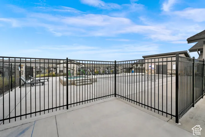 Paved patio area with a black metal fence enclosing a concrete pool deck and a raised spa