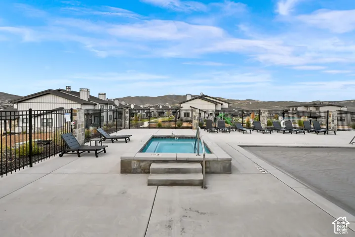 Outdoor spa with integrated steps, concrete hardscaping, and a surrounding black metal fence
