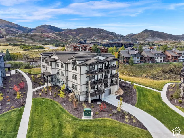 Multi-story building featuring stone and siding exterior, multiple private balconies, and a paved drive with integrated garage access