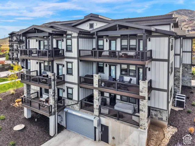 Multi-story residence featuring balconies with dark railings, stone columns, and light-colored siding