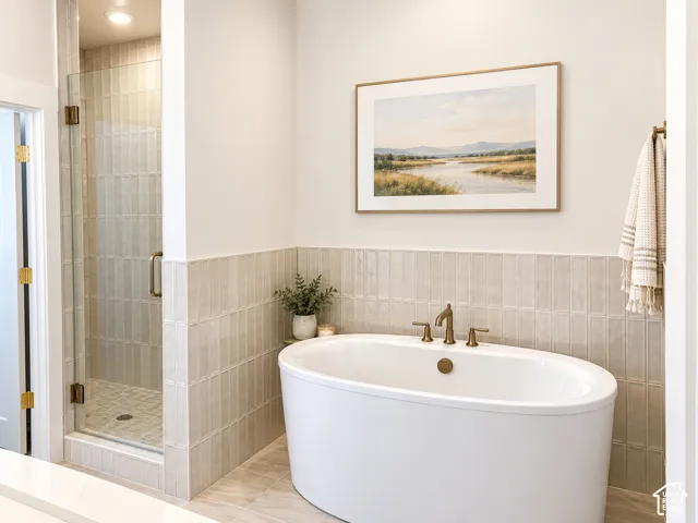Freestanding soaking tub with brass fixtures, glass-enclosed shower with tile surround, and vertical subway tile wainscoting