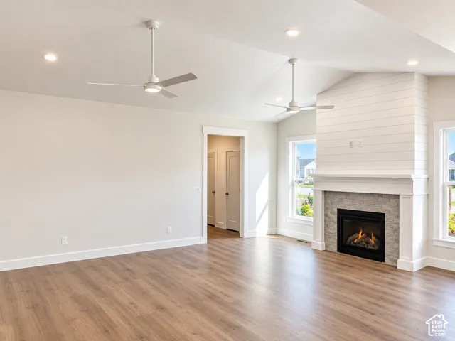 Vaulted ceiling with recessed lighting and ceiling fans, wood-finish flooring, and a fireplace with a stone surround and mantel