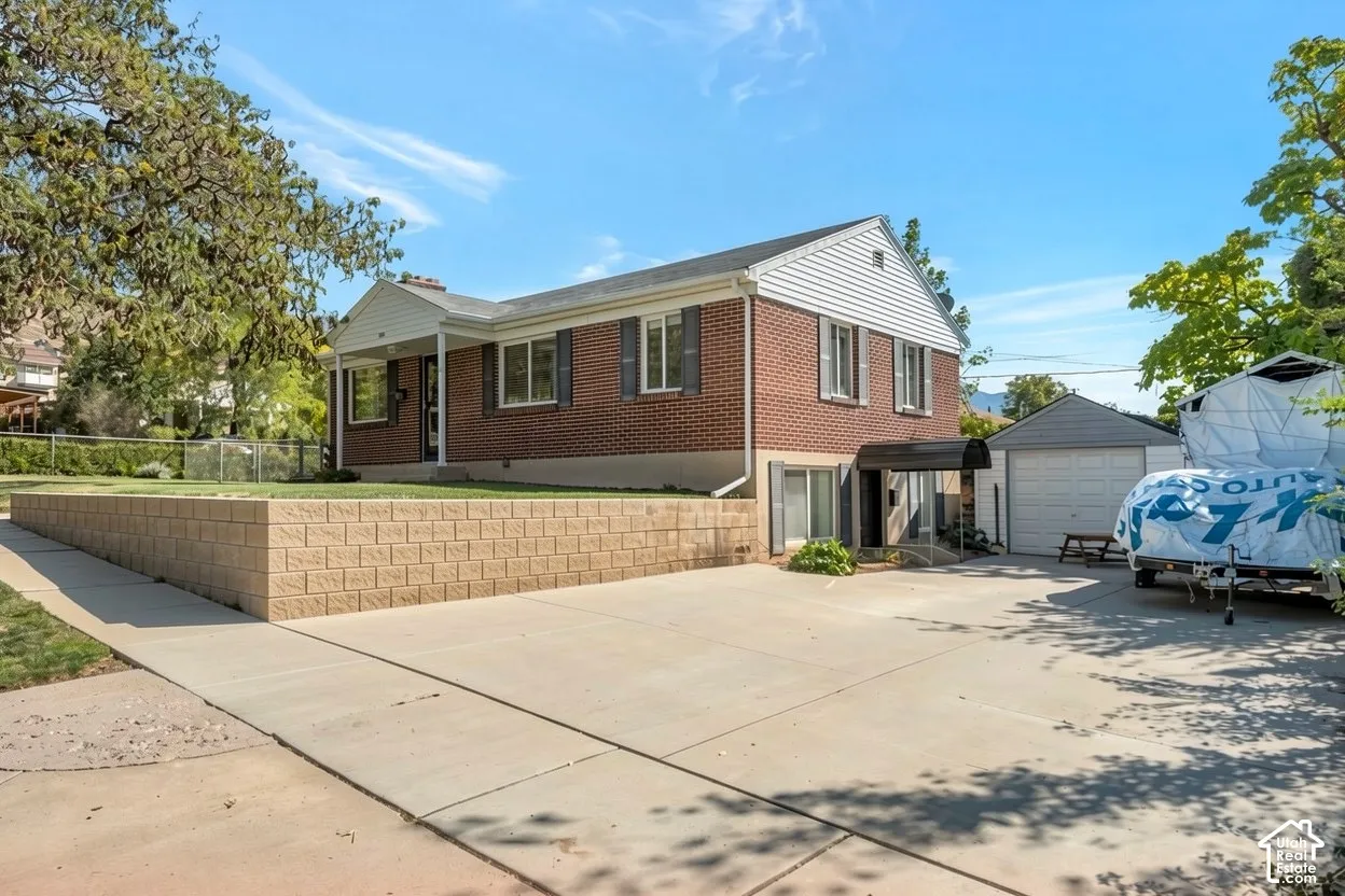 Brick and siding exterior, expansive concrete driveway, detached garage, covered patio entrance, and a terraced retaining wall