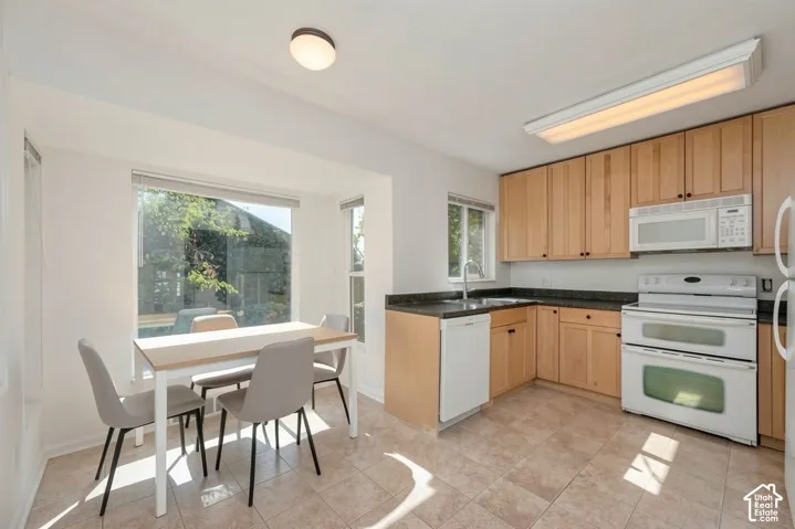 Kitchen featuring natural wood-finish cabinetry, dark countertops, white appliances, and tiled flooring