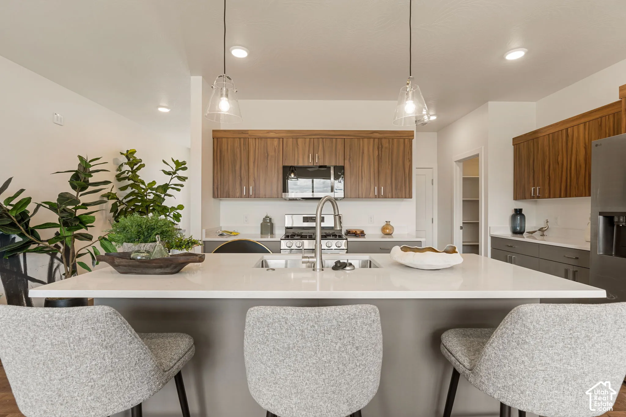 Modern kitchen featuring a waterfall-edge quartz countertop island, warm wood-finish cabinetry, stainless steel appliances, pendant lighting with glass shades, and seating for three at the island