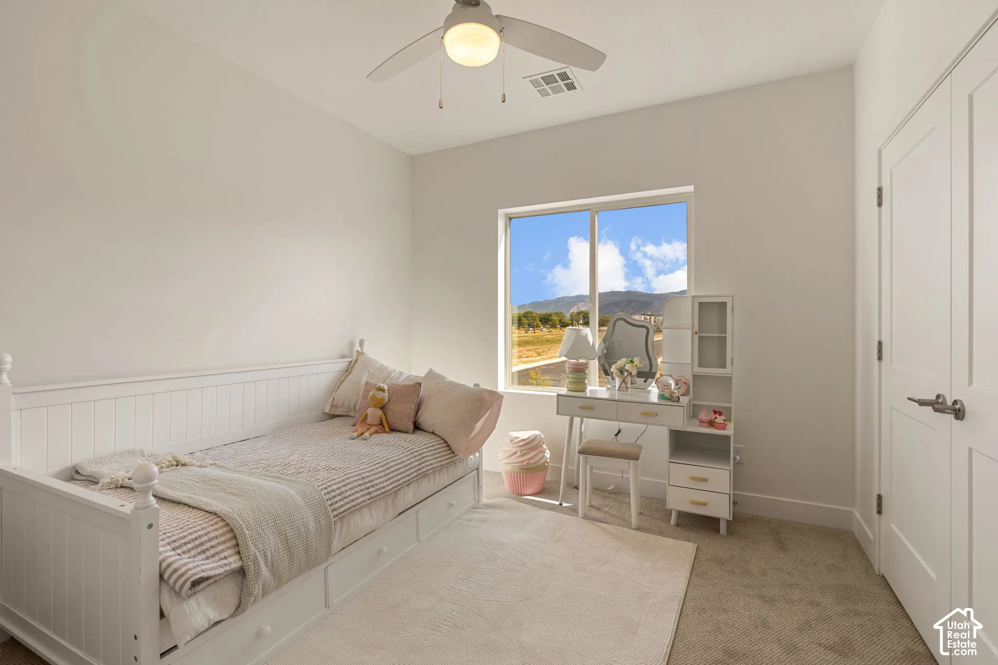 Bright bedroom featuring a large multi-pane window with natural light, carpeted flooring, and white wood-finish built-in cabinetry with shelving